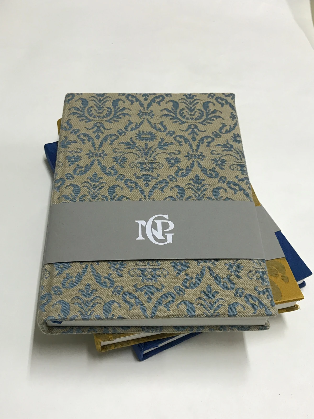 Patterned fabric journal with a branded grey sleeve and coloured ribbons