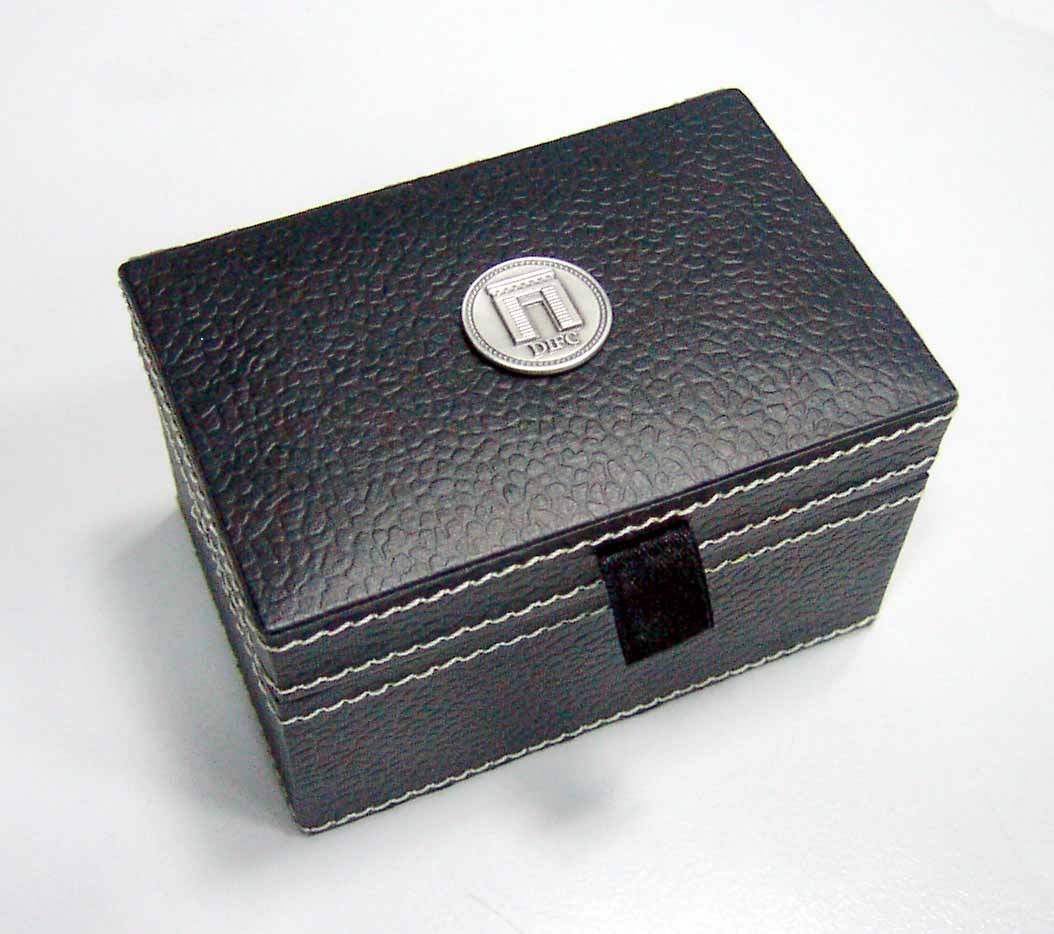Black textured presentation box with stitched edges and a metal badge