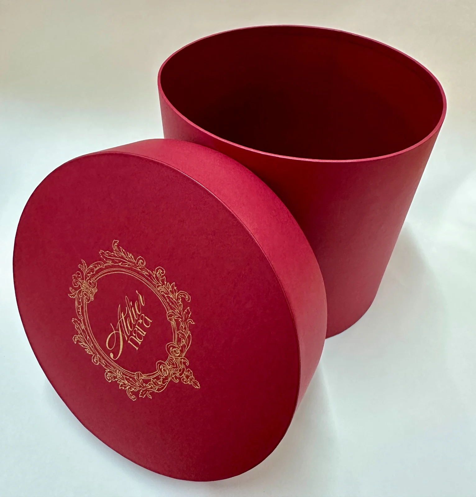 Open burgundy round box with gold decoration on its separate lid